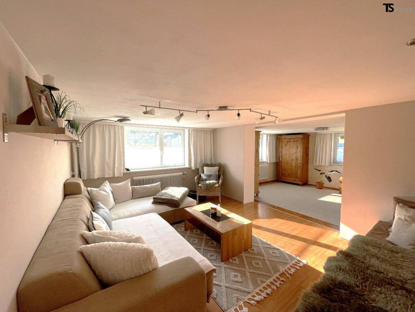 Helles Wohnzimmer mit großem Ecksofa, Holzboden und Blick ins Grüne durch die Fenster.