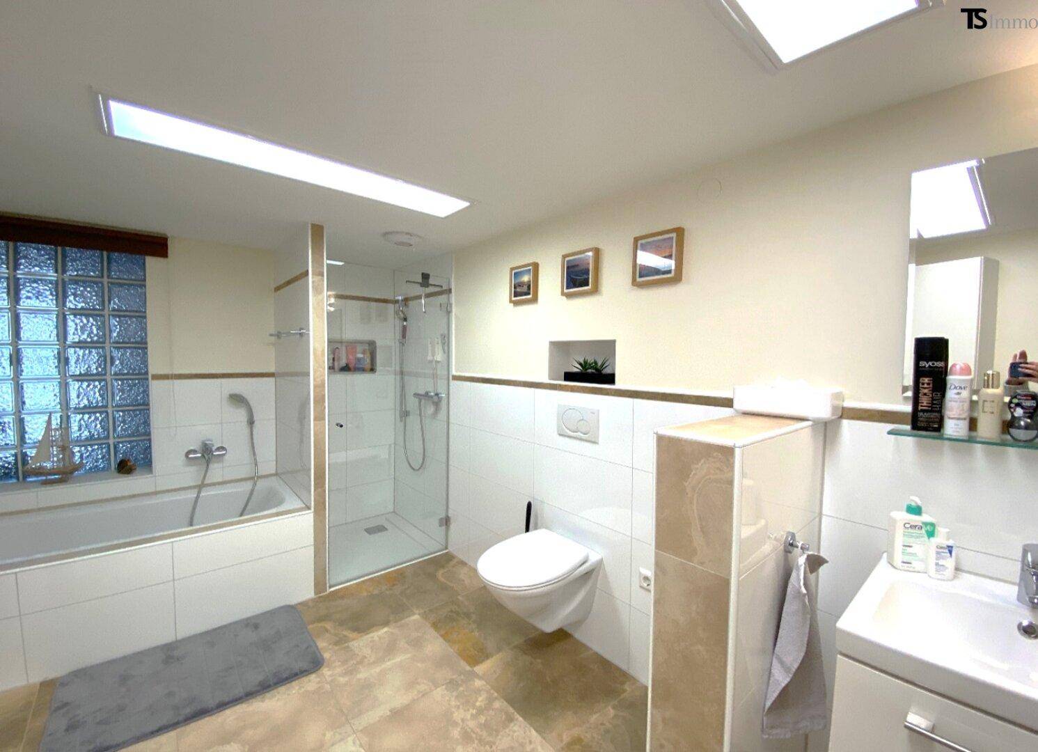 Helles Badezimmer mit Badewanne, begehbarer Dusche und Wand-WC.