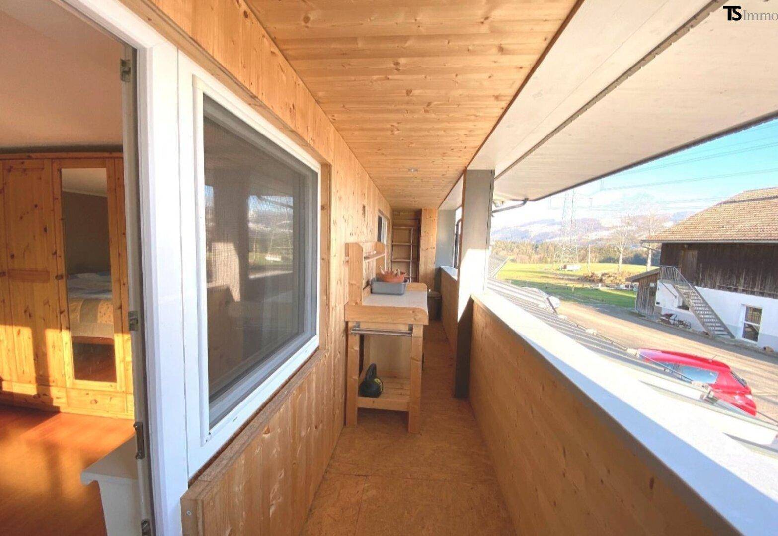Langer Holzbalkon mit Bergblick und viel Sonnenschein, ideal zum Entspannen im Freien.