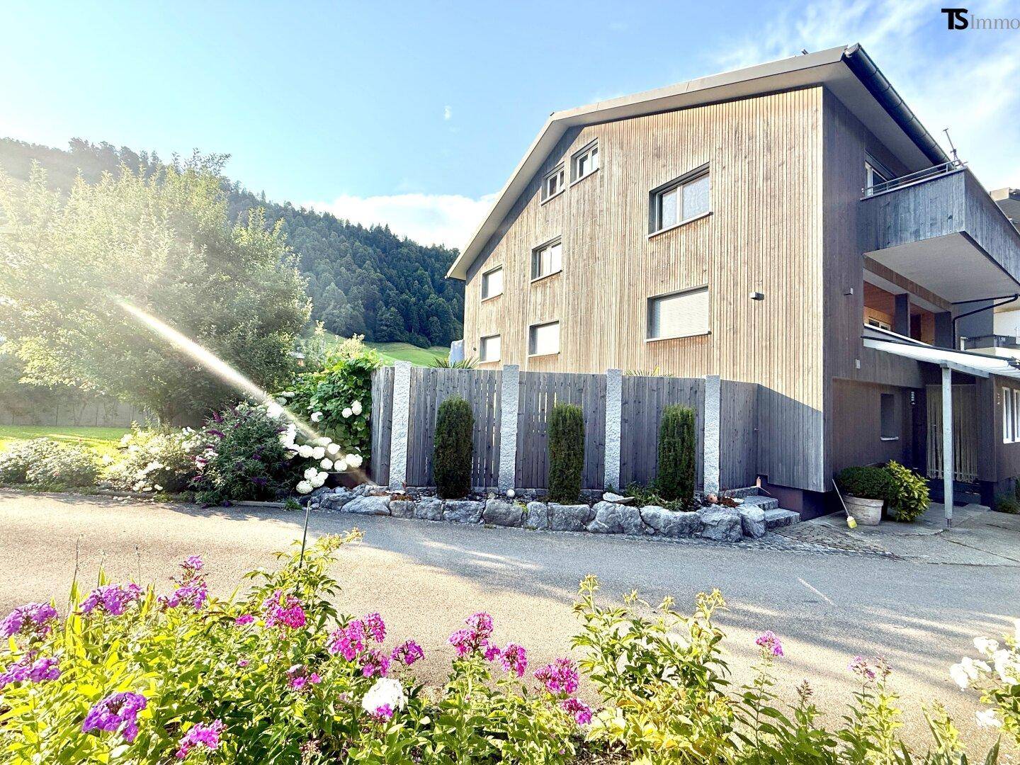Gepflegter Gartenbereich mit Blumenbeeten, Rasen und Bewässerungssystem vor dem Haus.