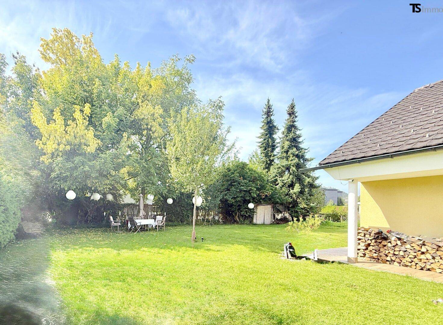 Großer, sonniger Garten mit altem Baumbestand und Essbereich im Freien.