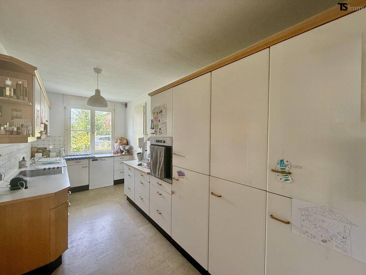 Funktionale Küche mit weißen Schränken, Holzdetails und Fenster zum Garten.