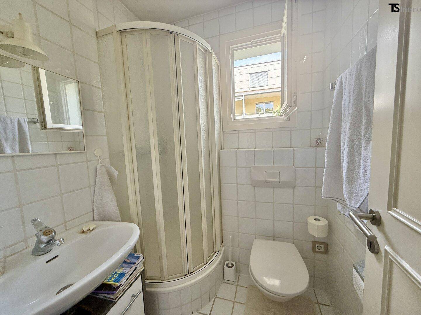 Kleines Badezimmer mit Dusche, WC, Waschbecken und Fenster.