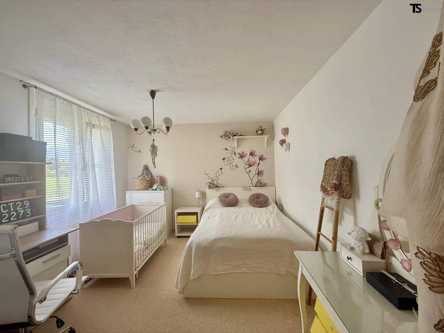 Kinderzimmer mit hellem Teppichboden, Babybett und floraler Wanddekoration.
