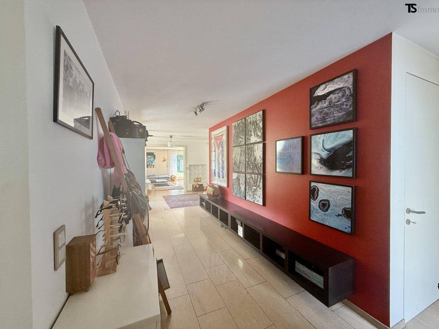 Langer Flur mit roter Akzentwand, Fliesenboden und moderner Kunst.