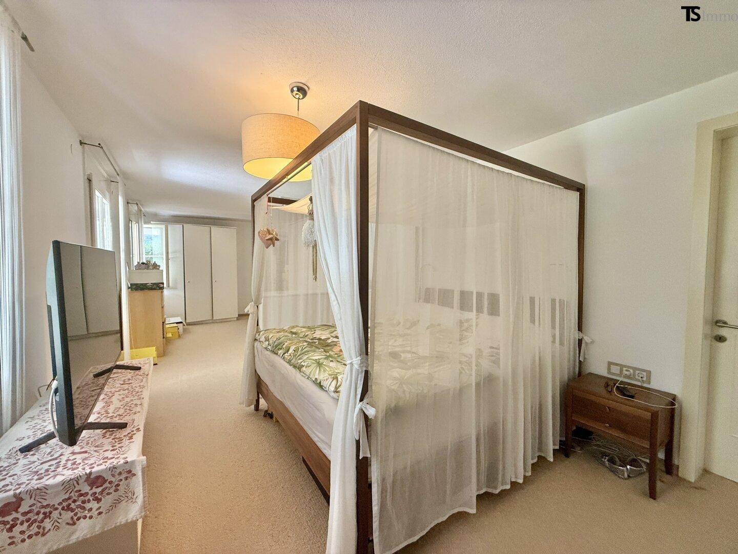 Geräumiges Schlafzimmer mit Himmelbett, Teppichboden und viel Tageslicht.