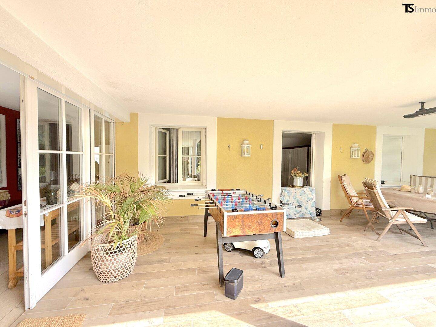 Helle, überdachte Terrasse mit großen Glastüren zum Innenbereich und Tischfußball.