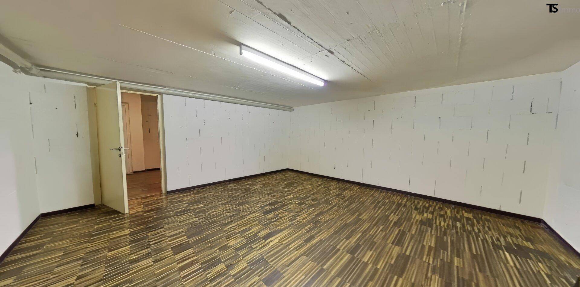 Geräumiger Kellerraum mit weiß gestrichenen Wänden, Holzboden und einfacher Beleuchtung.