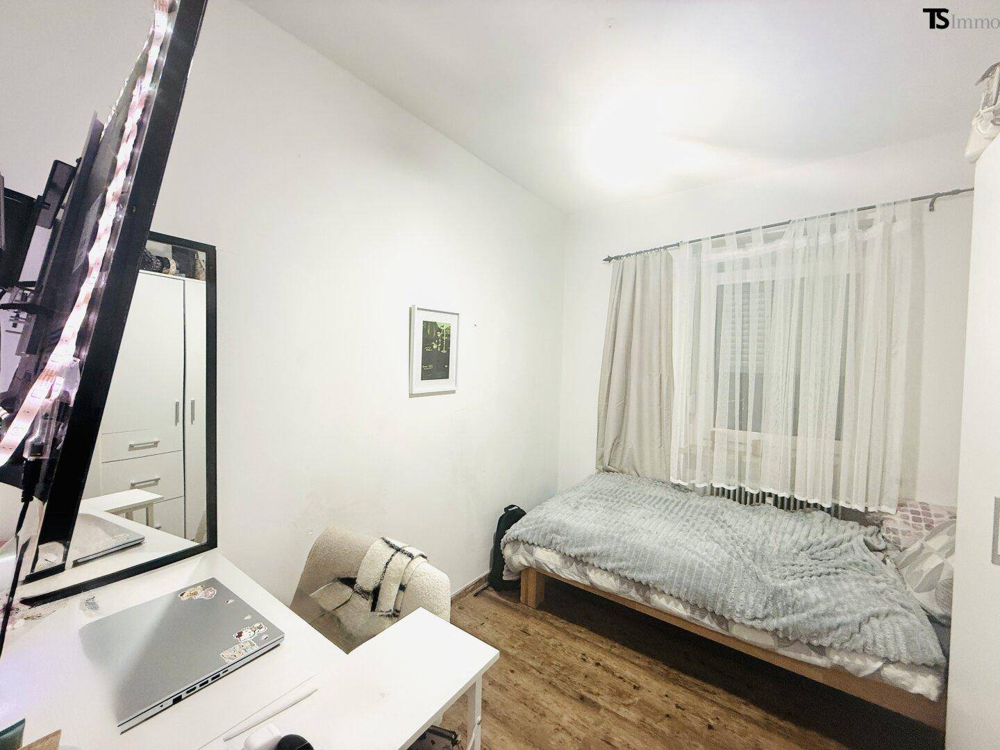 Gemütliches Schlafzimmer mit Einzelbett, Schreibtisch und hellem Holzfußboden.