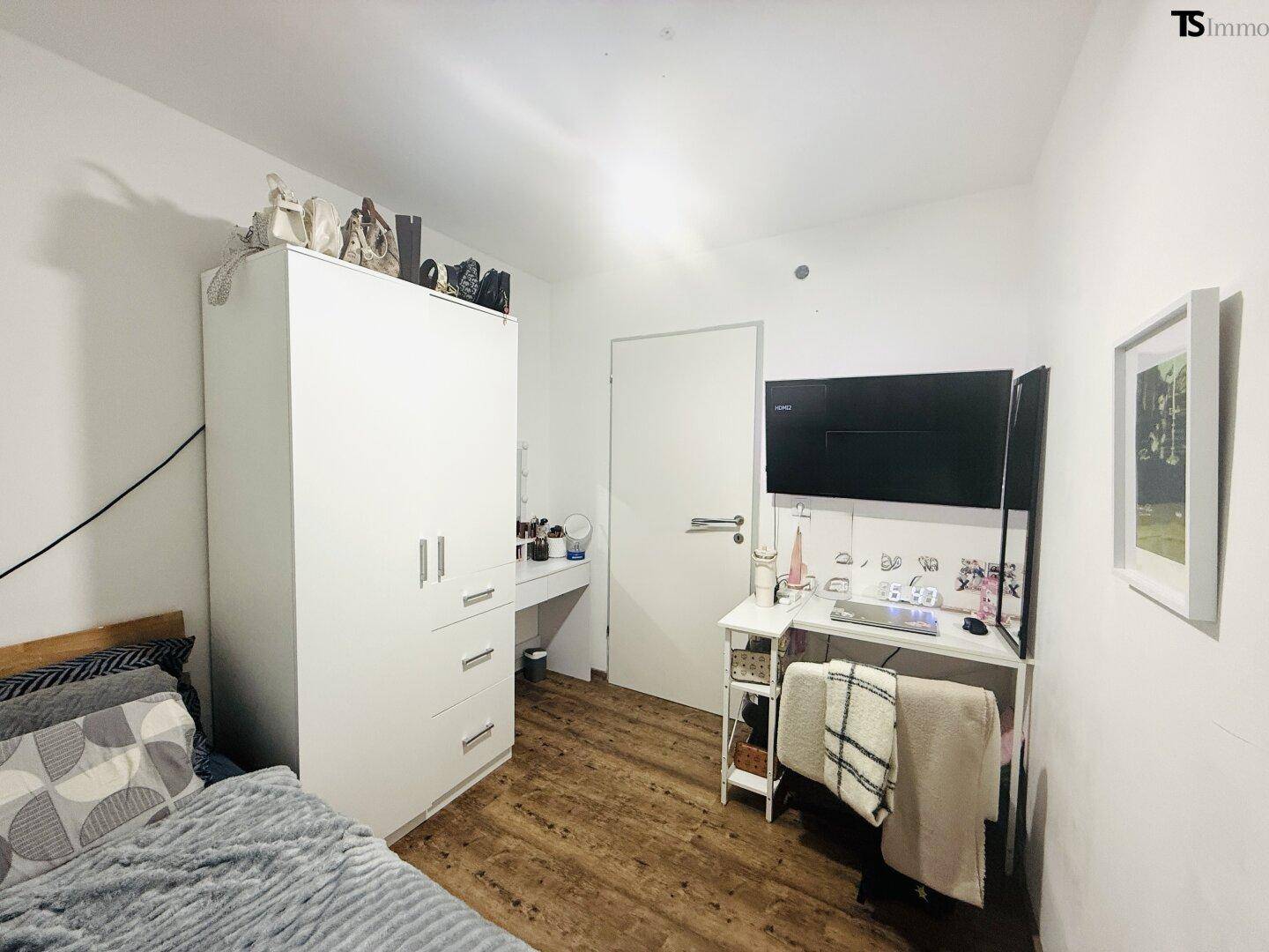 Funktionales Schlafzimmer mit weißem Kleiderschrank, Schreibtisch und hellem Ambiente.