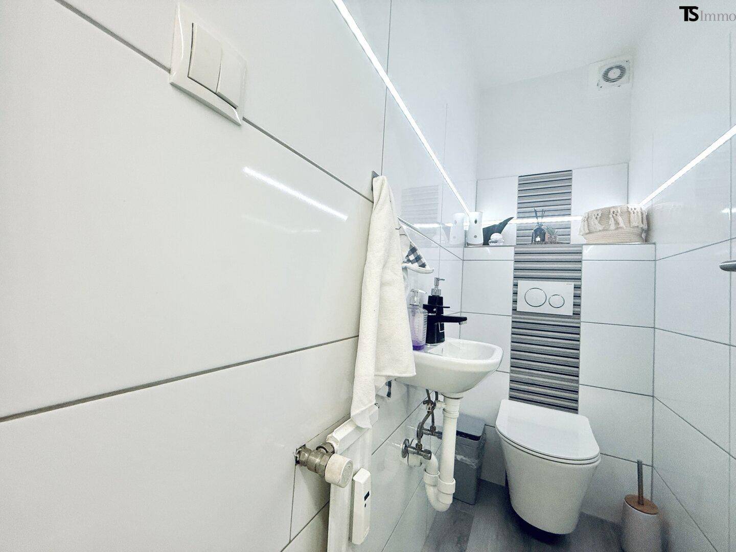 Helles Gäste-WC mit wandhängendem WC und kleinem Waschbecken, modern gefliest.