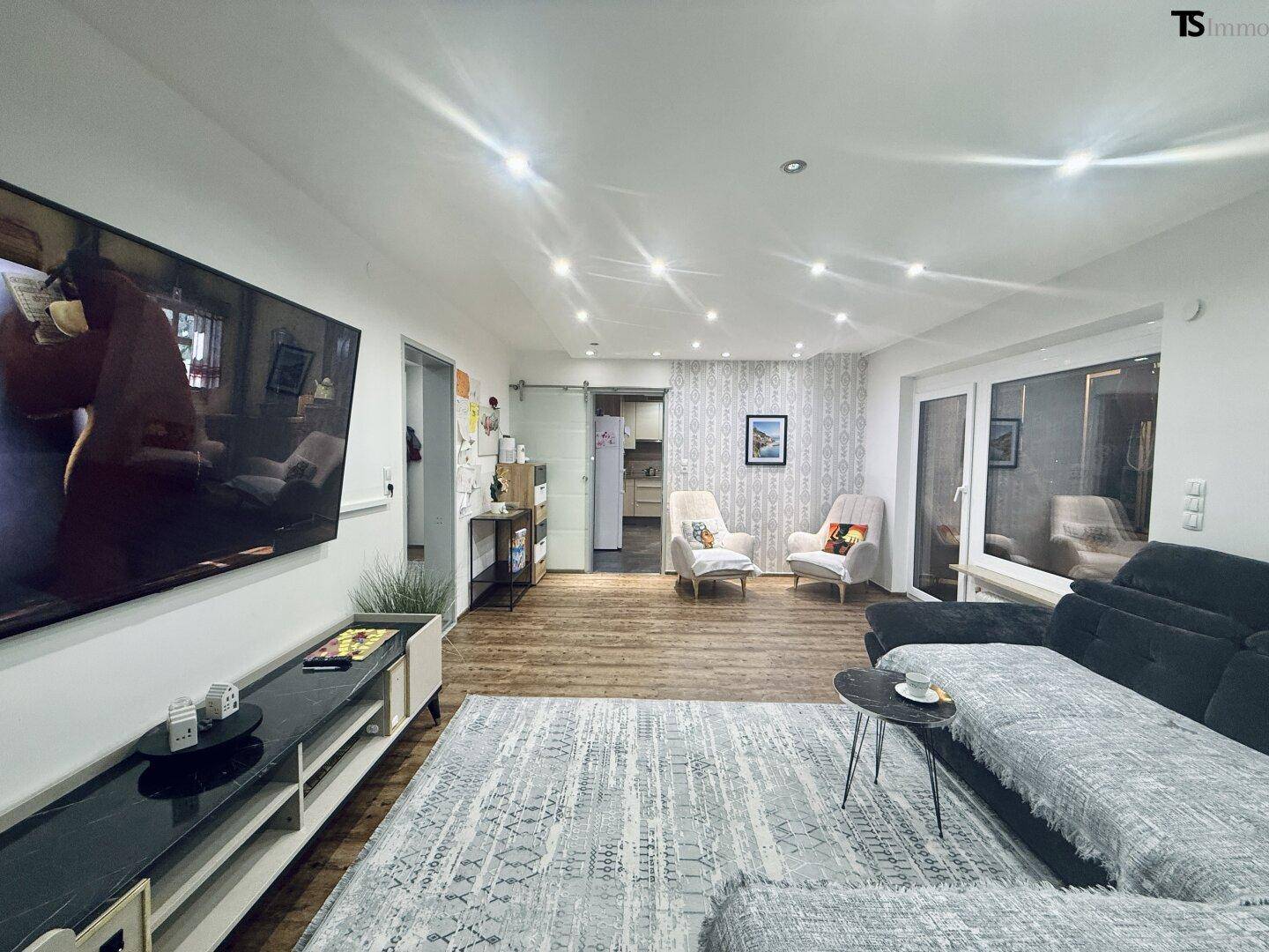 Helles Wohnzimmer mit Zugang zum Balkon, großem Sofa und modernem Unterhaltungssystem.