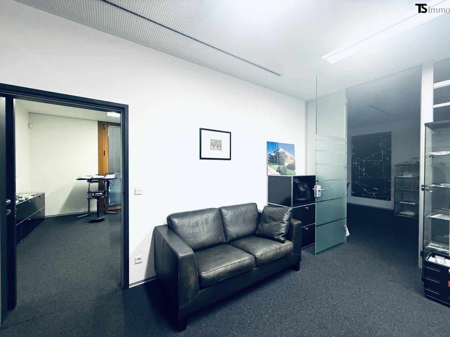 Gemütlicher Wartebereich mit Ledersofa und Kunstwerken an der Wand, angrenzend an Büroräume.