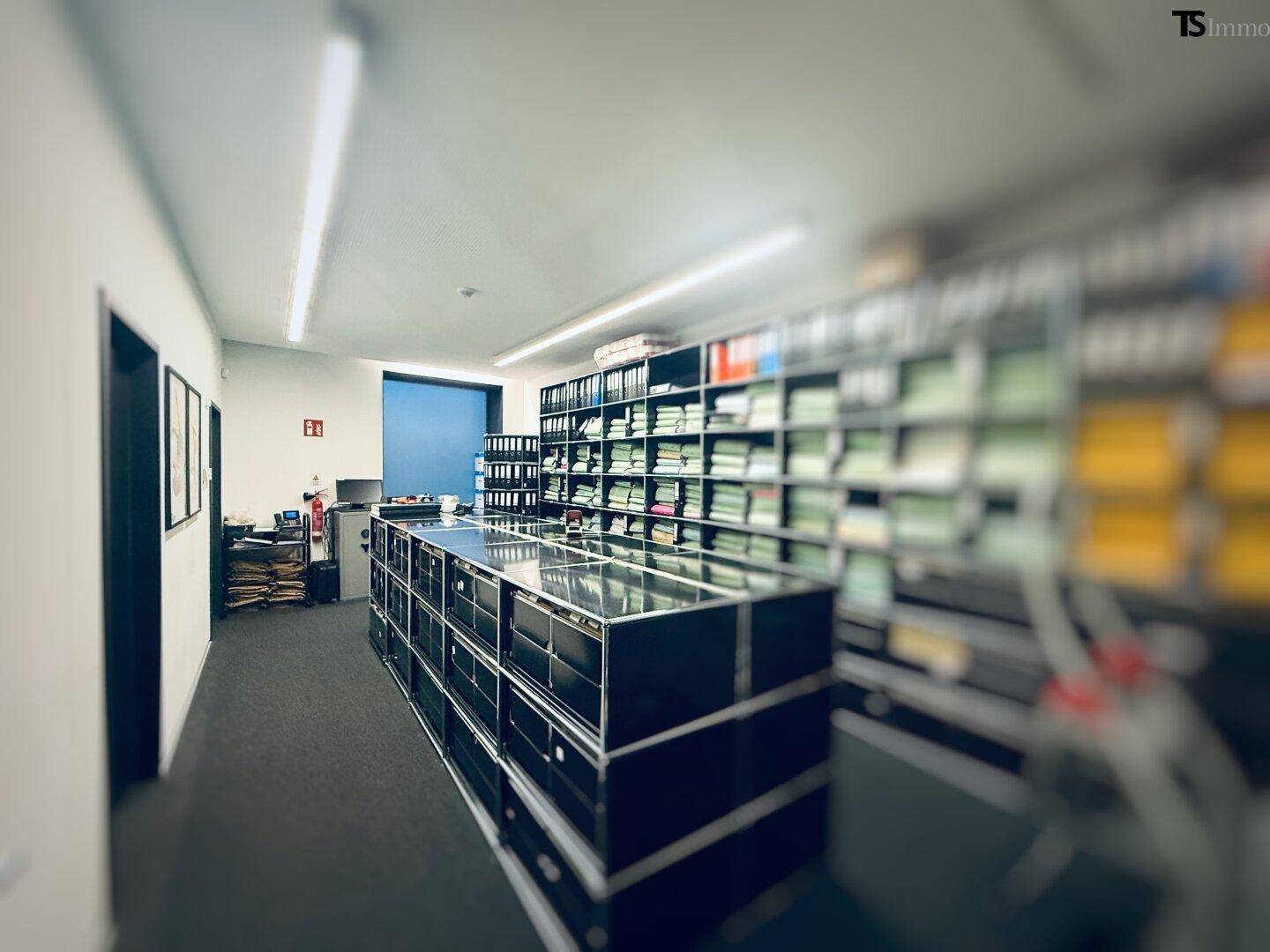 Weiterer Archivbereich mit umfangreichen Regalsystemen und einem Schreibtisch am Ende des Raumes.