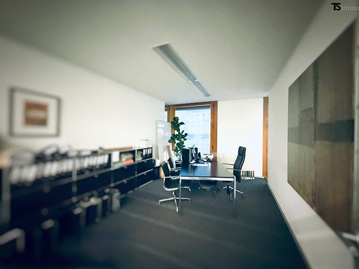 Einzelbüro mit Schreibtisch, Bürostuhl und Regalen, beleuchtet durch ein großes Fenster.