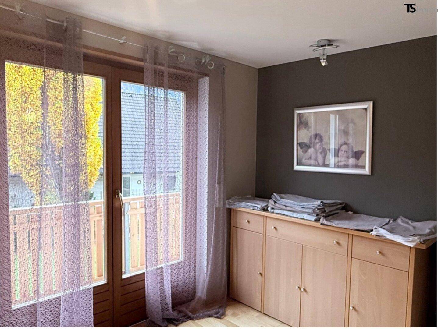 Schlafzimmer mit Holzboden, Kommode und Zugang zu einem französischen Balkon.