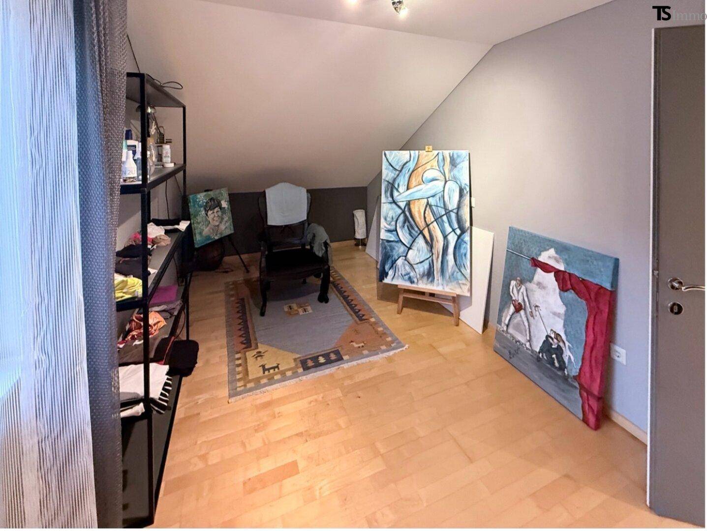 Dachgeschosszimmer mit Holzboden, schrägen Wänden und Kunstwerken.