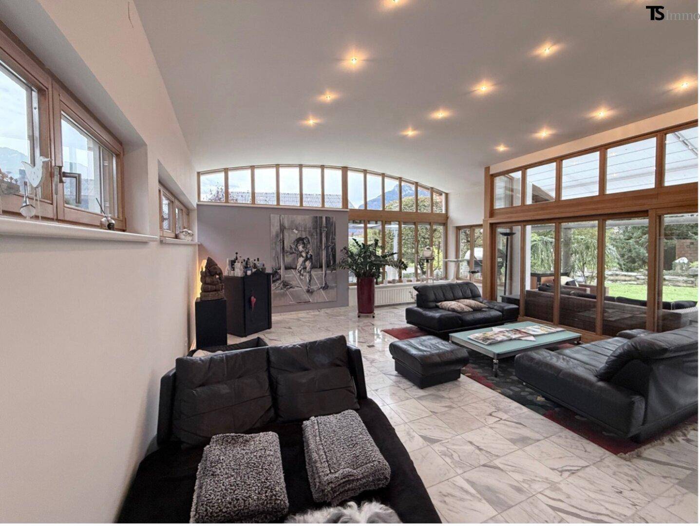 Großzügiges Wohnzimmer mit Marmorboden, vielen Fenstern und Blick in den Garten.