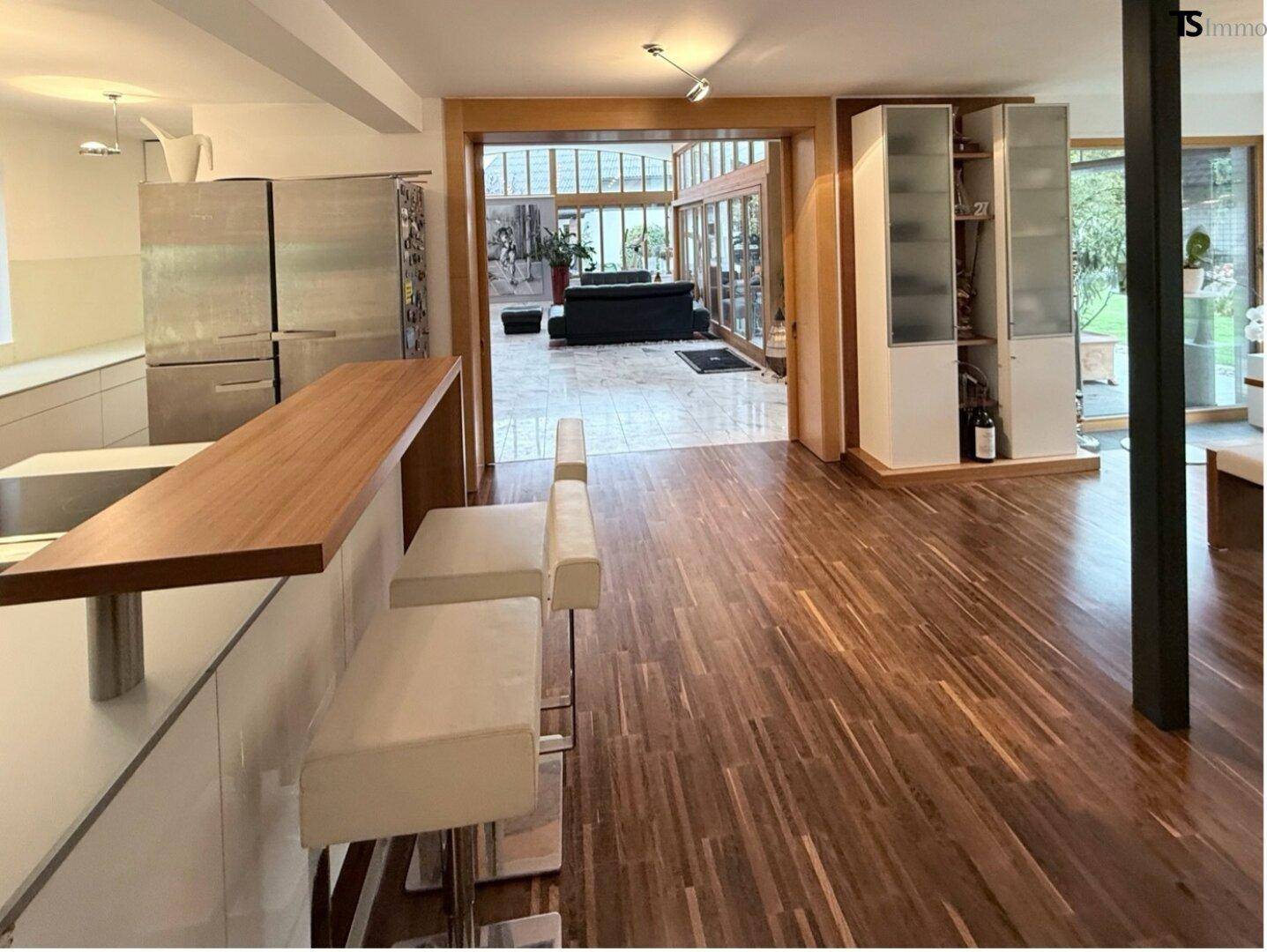 Moderne Küche mit Holzboden und Frühstücksbar, offen zum Essbereich.
