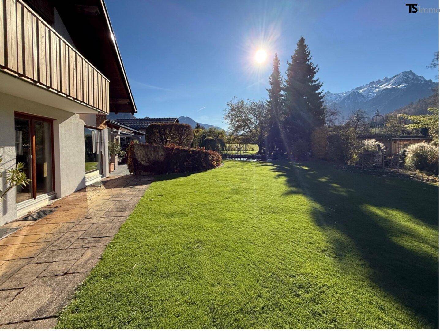 Sonniger Gartenbereich mit Rasenfläche, Terrasse und Bergblick.
