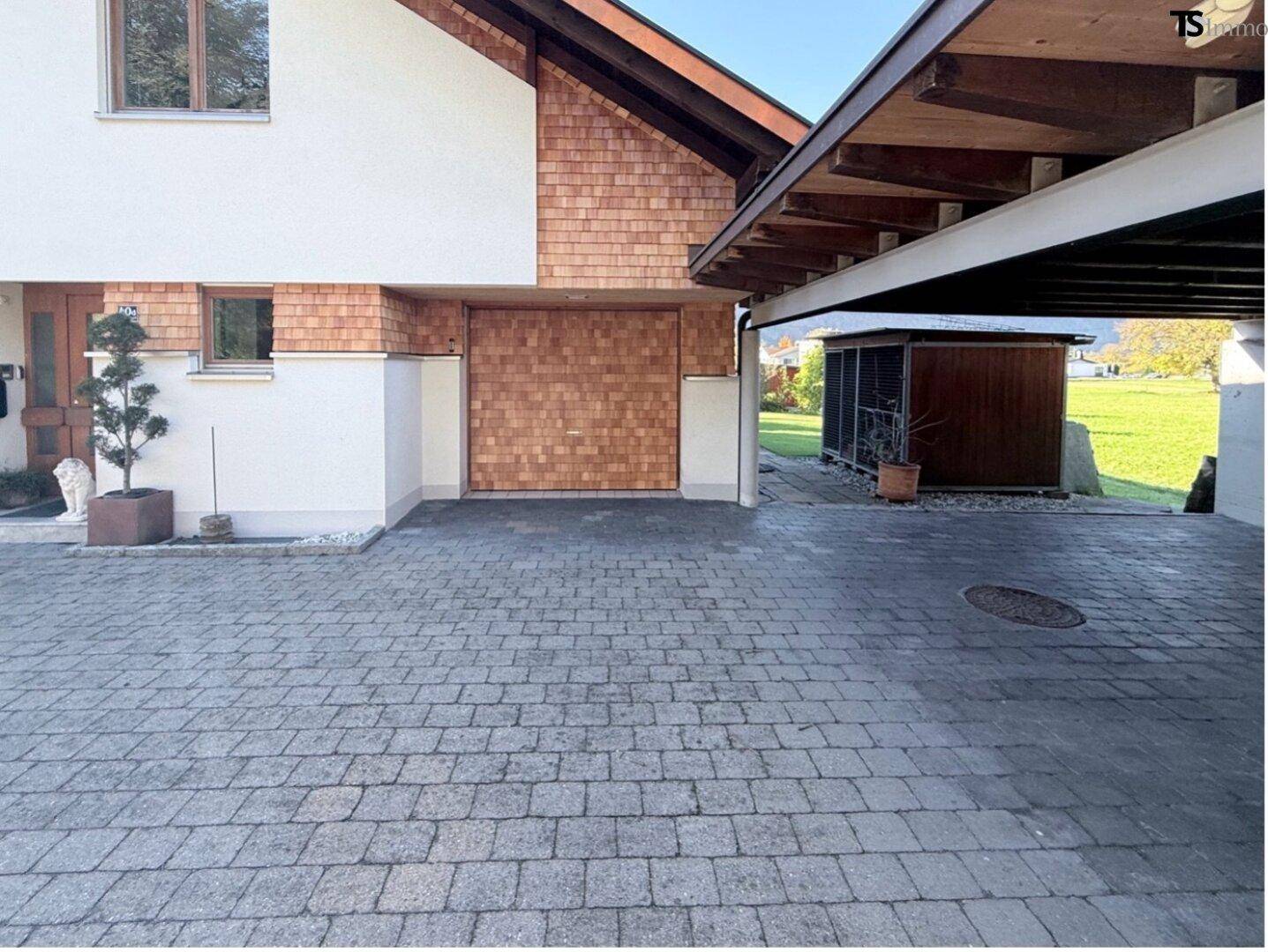 Gepflasterte Auffahrt mit Carport und Zugang zur Garage.