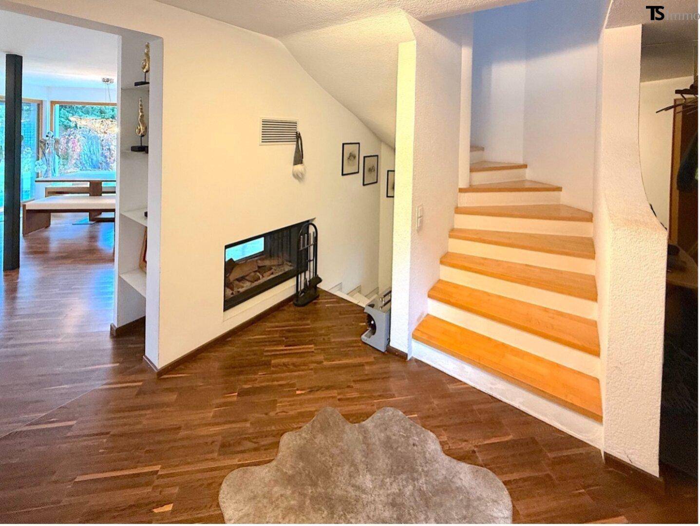 Heller Flur mit Holztreppe, Kamin und Zugang zu weiteren Räumen.