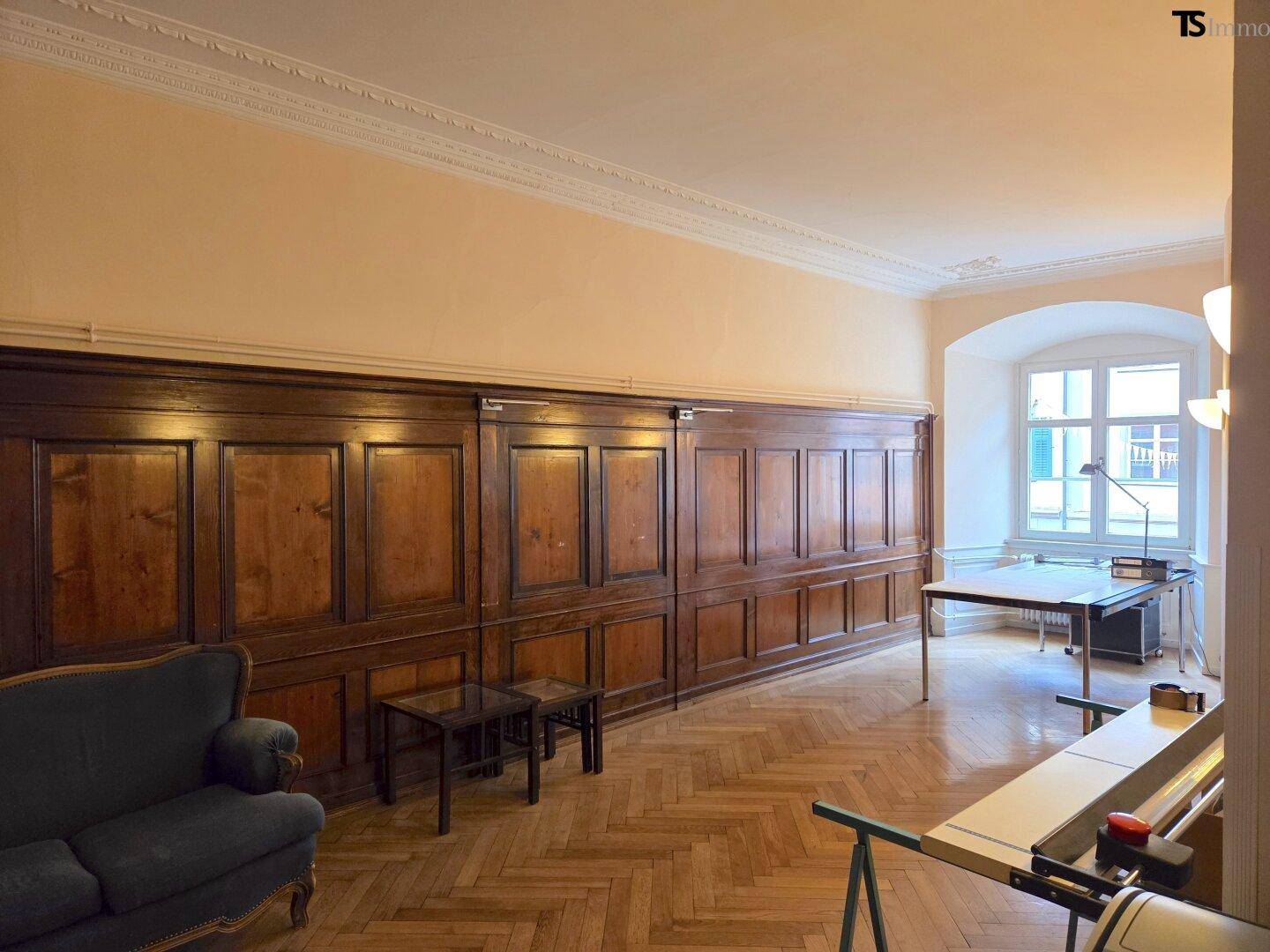 Geräumiges Büro mit eleganter Holzvertäfelung, Fischgrätparkett und hohen Fenstern, ideal für repräsentative Zwecke.