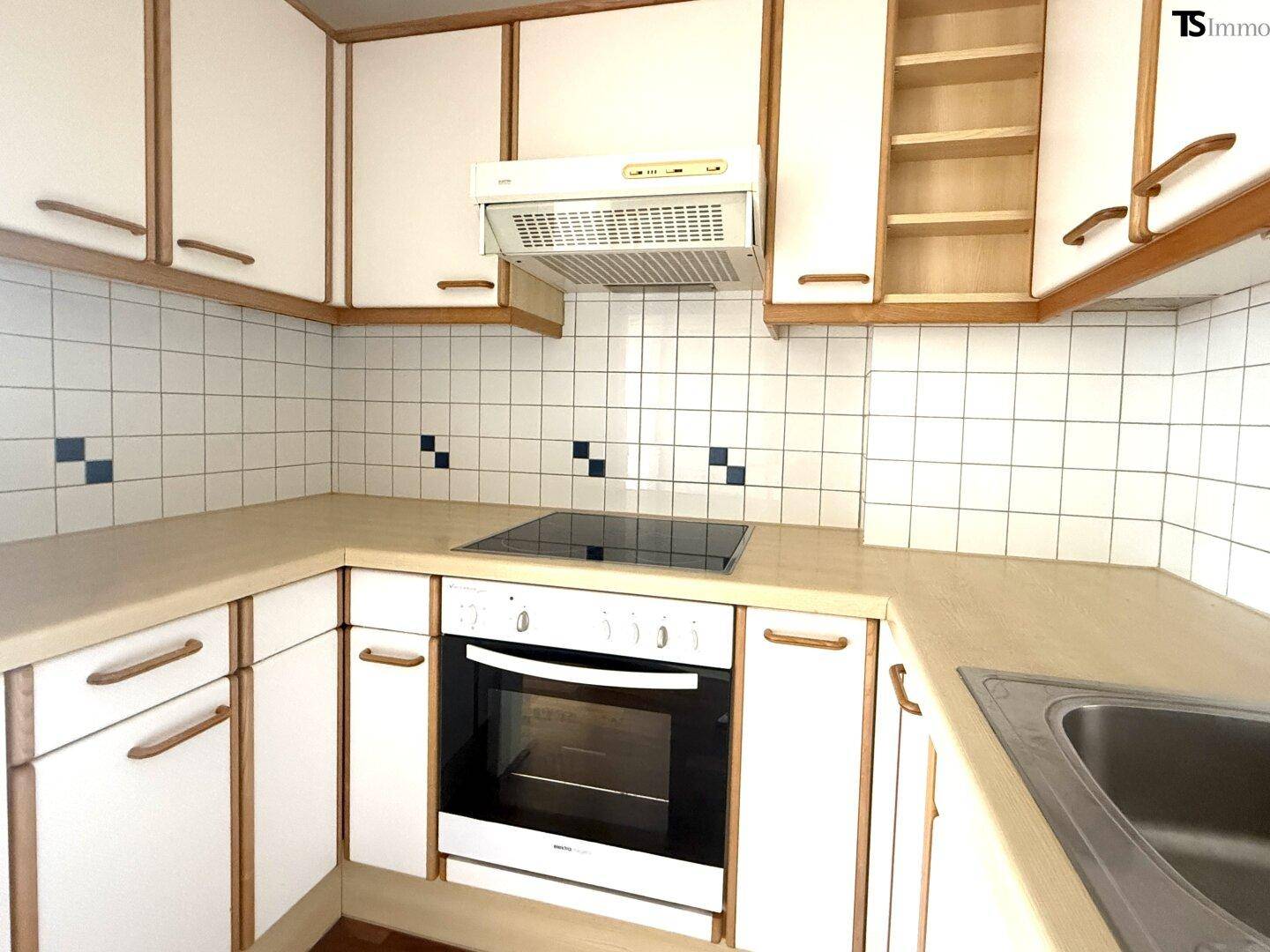 Funktionale Küche mit weißen Schränken, hellen Arbeitsplatten und integriertem Backofen und Kochfeld.