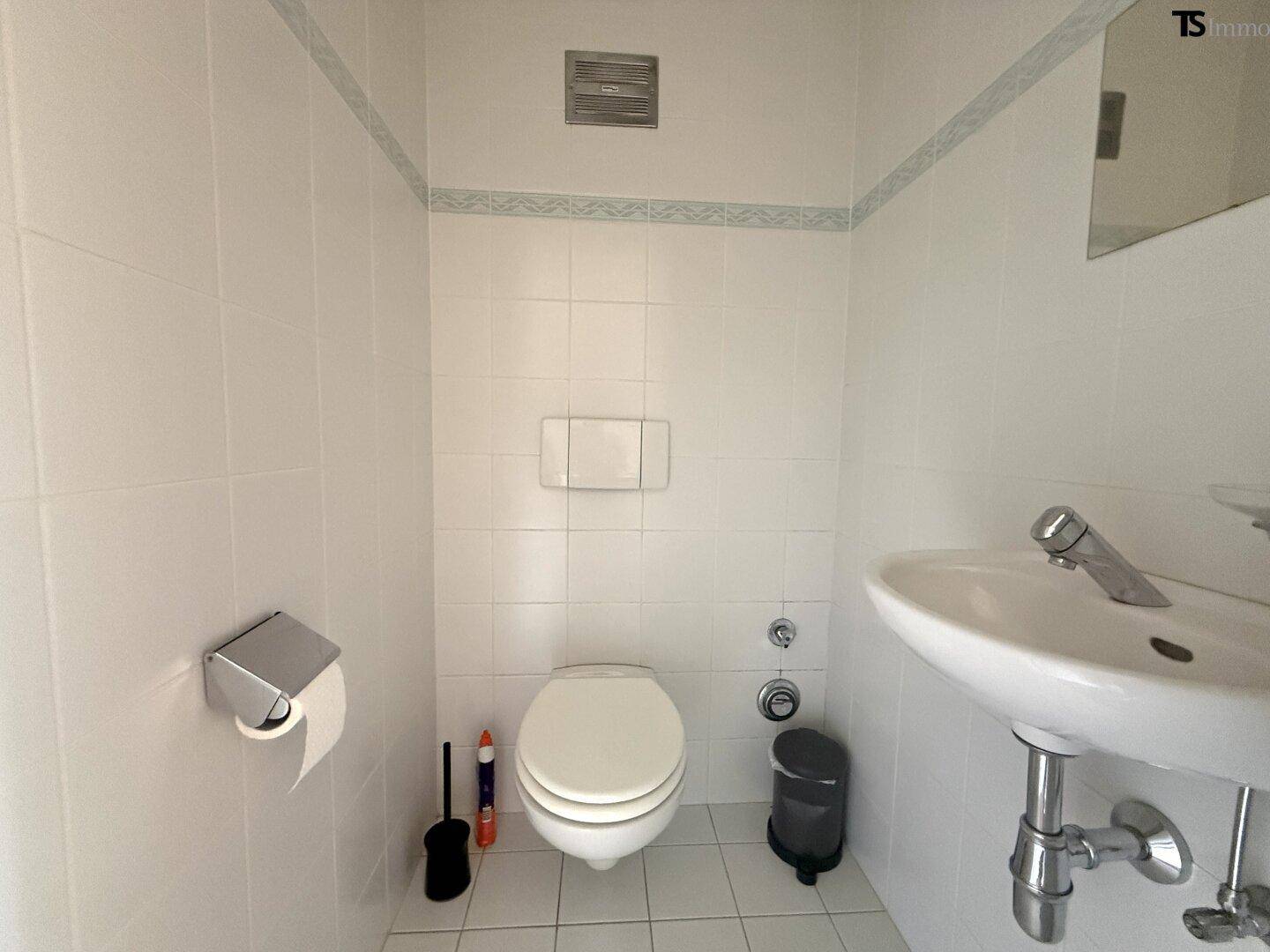 Separates Gäste-WC mit weißen Fliesen, wandhängender Toilette und kleinem Waschbecken.