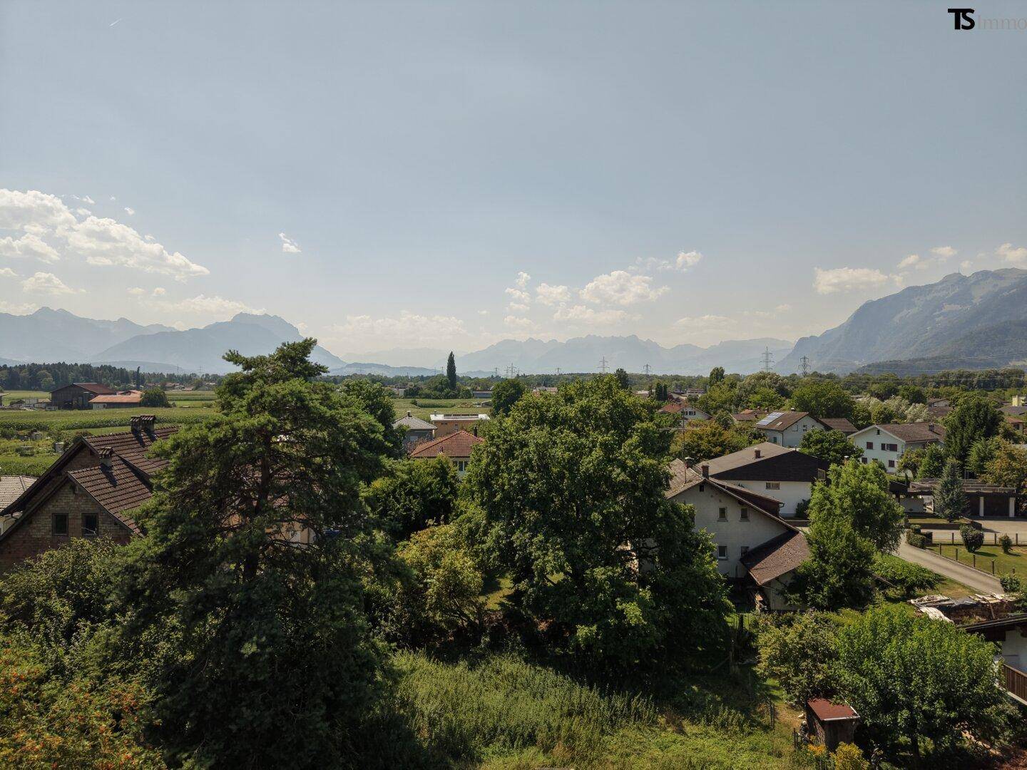 Weitläufiger Blick über die Wohnsiedlung mit üppigem Grün und majestätischen Bergen im Hintergrund.