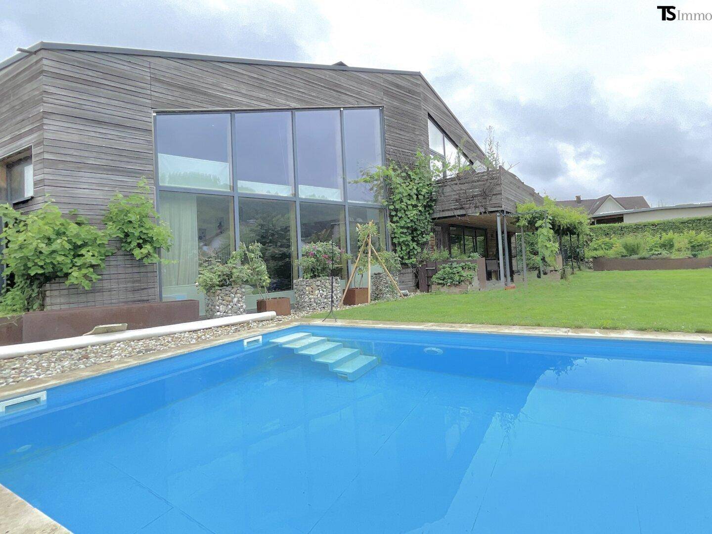 Ansicht des modernen Hauses mit großem Pool und weitläufigem Gartenbereich an einem bewölkten Tag.
