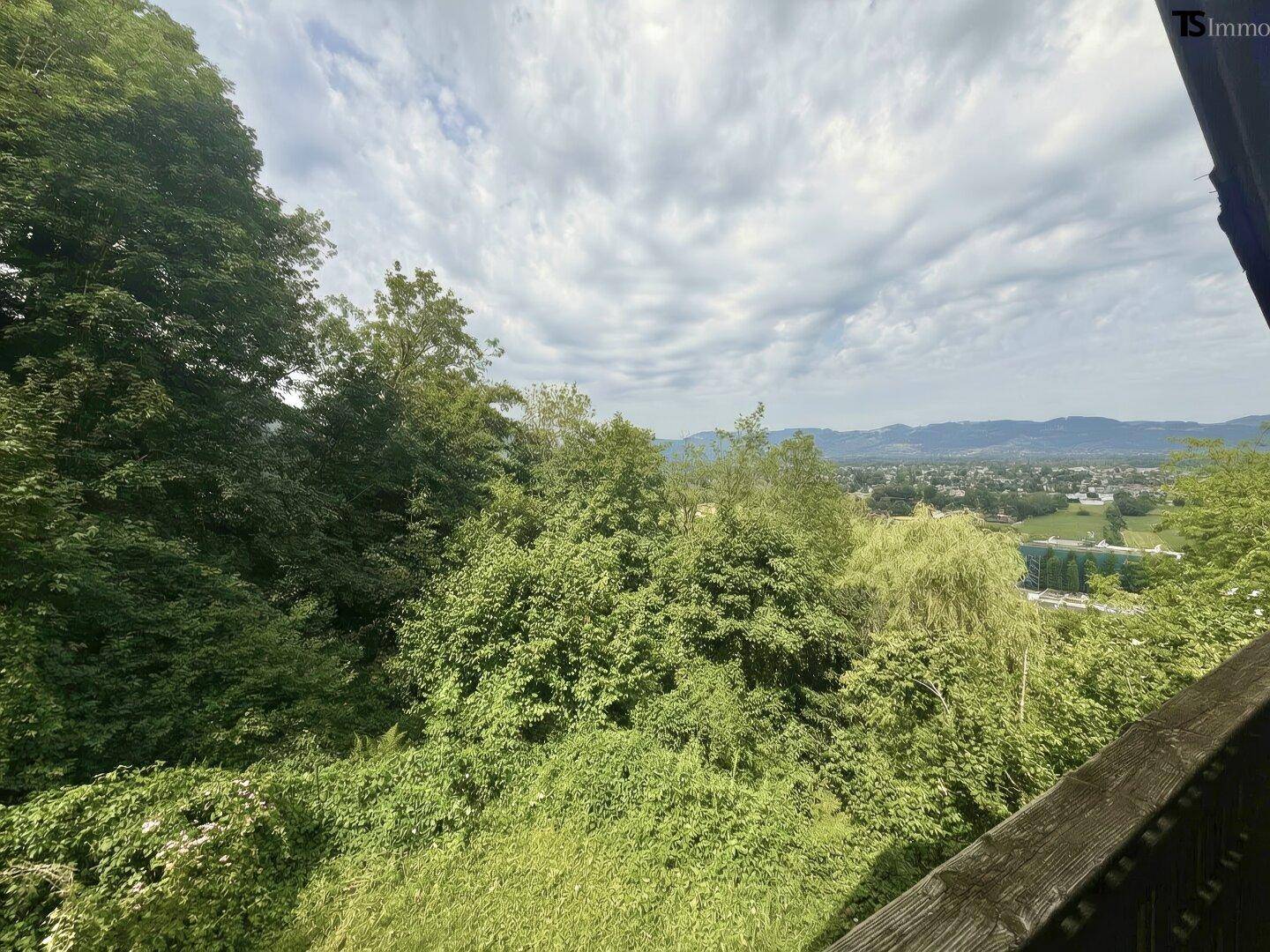 Balkon mit weitem Blick über grüne Hügel und die umliegende Landschaft unter bewölktem Himmel.