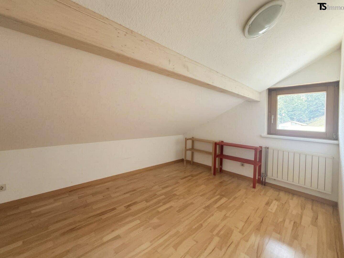 Helles Dachzimmer mit Holzboden, Dachschräge und Fenster mit Blick ins Grüne.