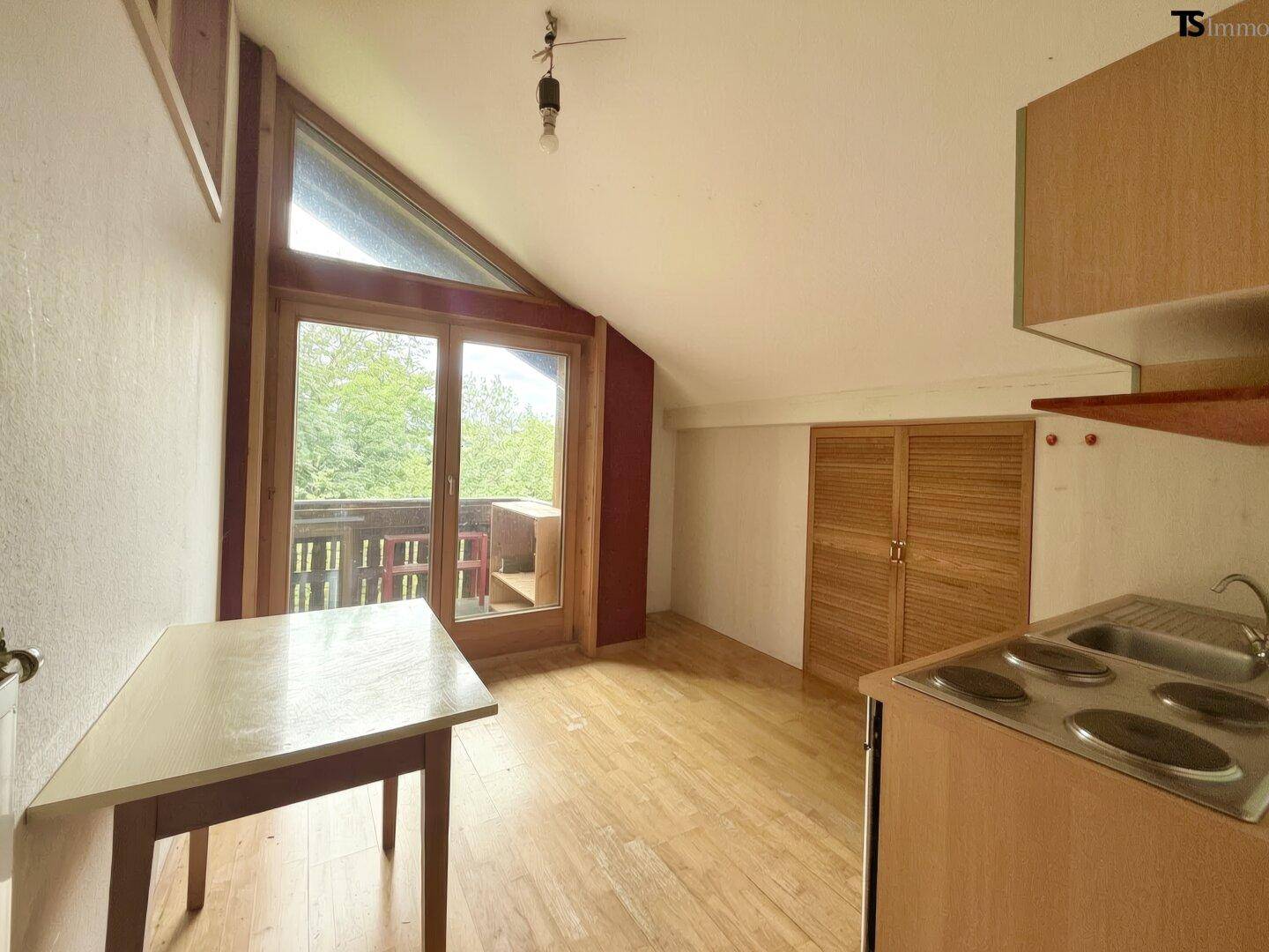 Dachbodenraum mit kleiner Küchenzeile, Holzboden und Balkonzugang, ideal als Studio.
