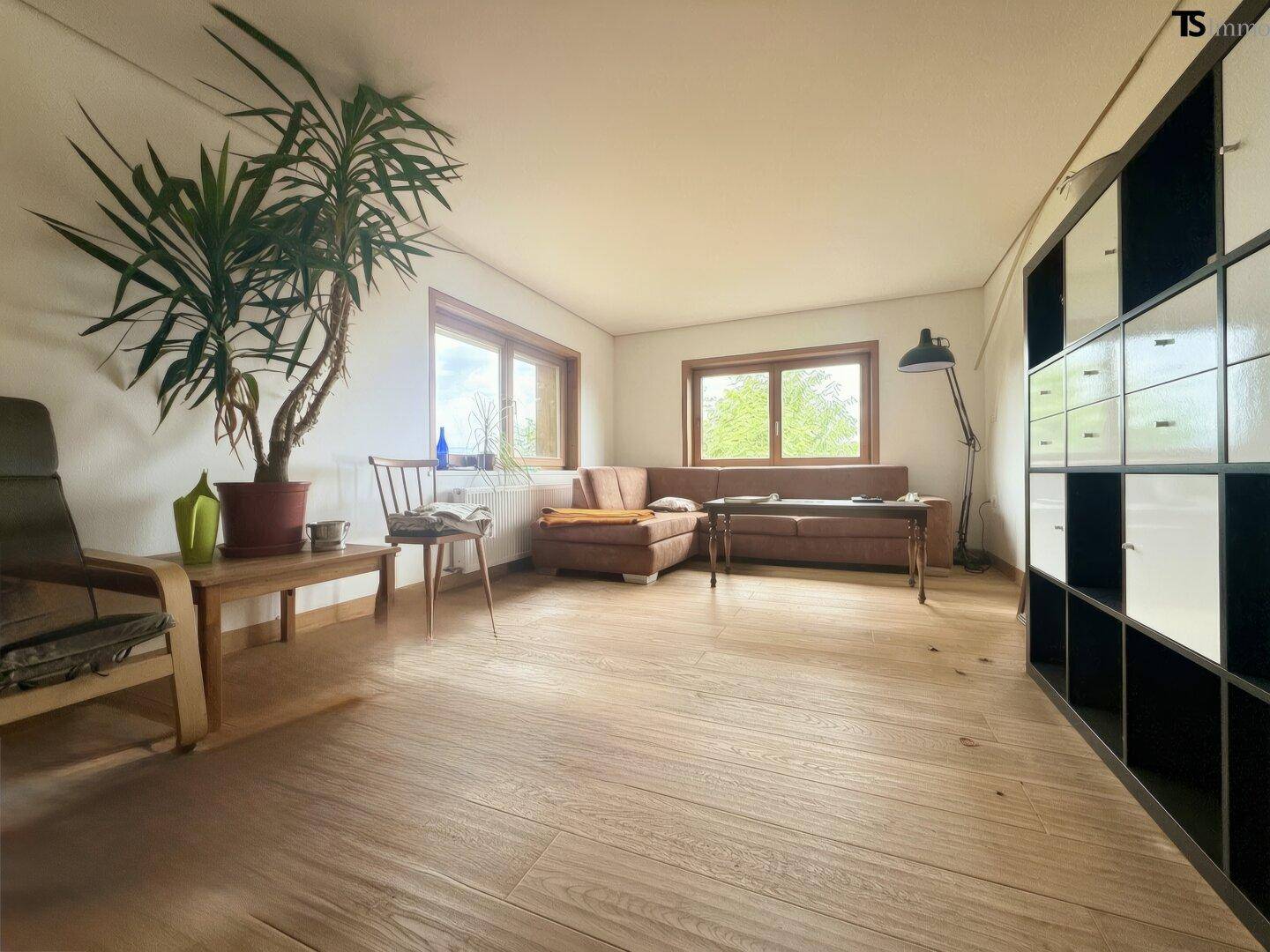 Geräumiges Wohnzimmer mit Holzboden, großen Fenstern und viel Tageslicht, modern eingerichtet.