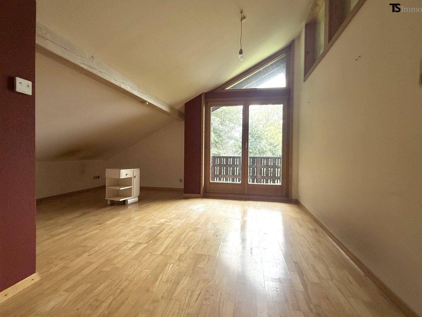 Heller Dachbodenraum mit Holzboden, Dachschräge und Zugang zu einem kleinen Balkon.