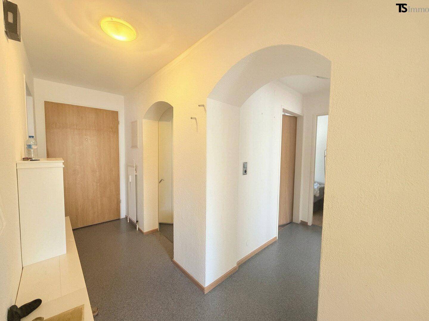 Heller Flur mit grauen Bodenfliesen und Rundbögen, verbindet verschiedene Räume der Wohnung.