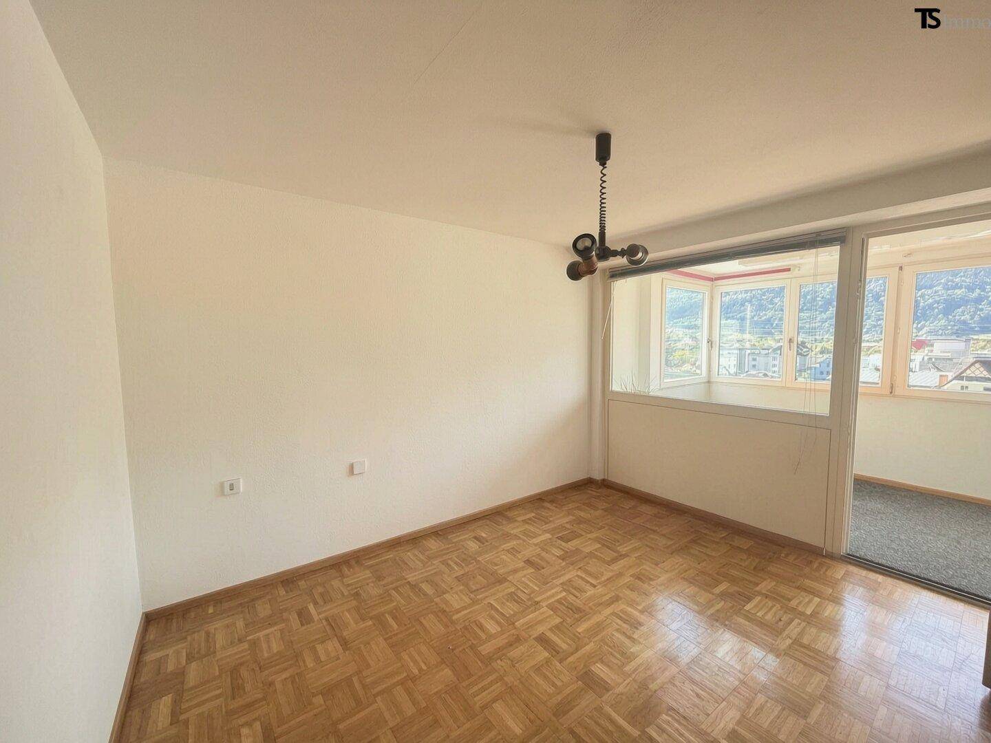 Leeres Zimmer mit Parkettboden und weiß gestrichenen Wänden, mit Zugang zu einem Nebenraum.
