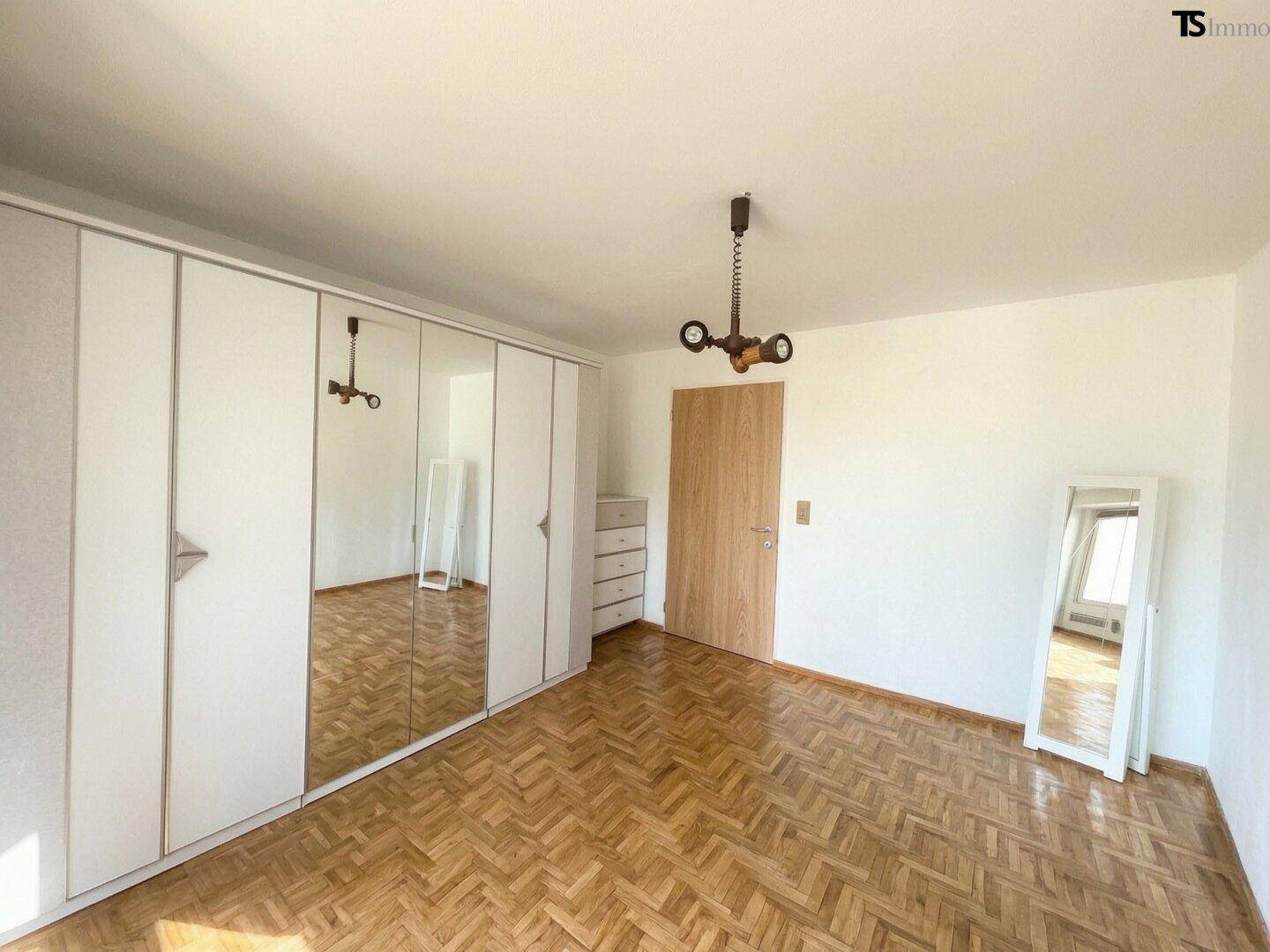 Schlafzimmer mit weißen Einbauschränken, Spiegeltüren und Fischgrätparkett, bietet viel Stauraum.