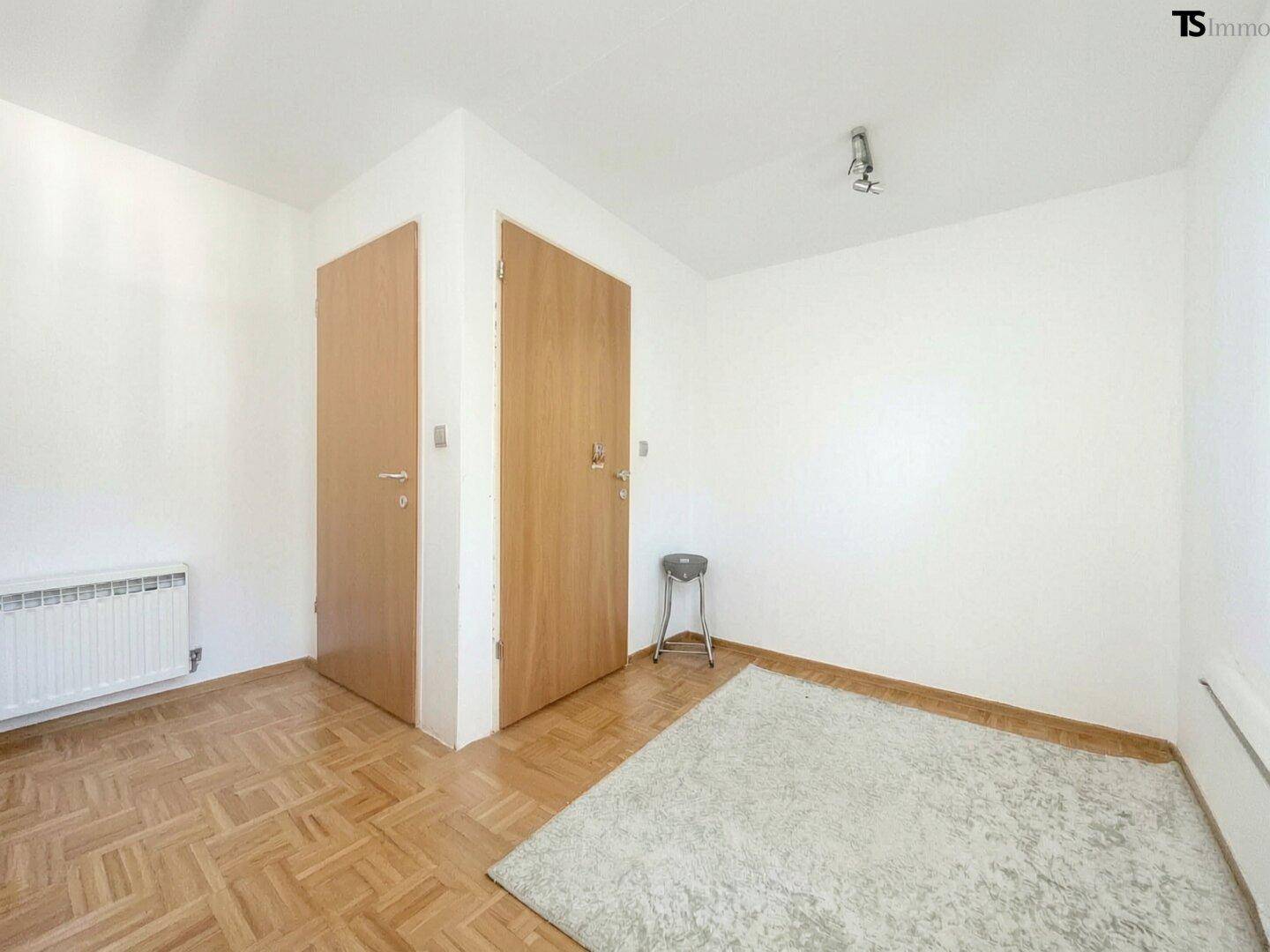 Leeres Zimmer mit Parkettboden und zwei Holztüren, bietet flexible Nutzungsmöglichkeiten.