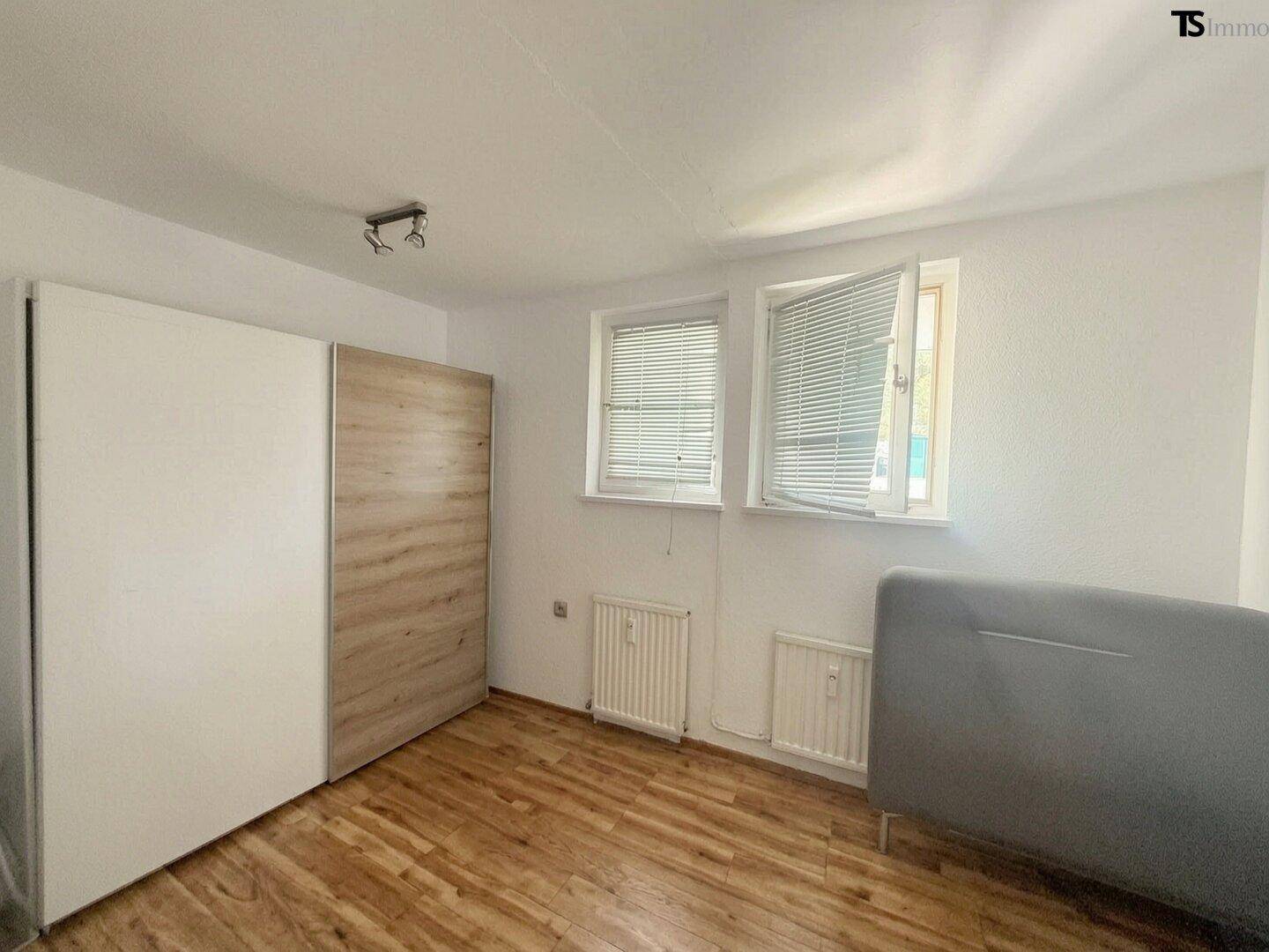 Schlafzimmer mit Parkettboden, weißem Kleiderschrank und zwei Fenstern, hell und funktional.