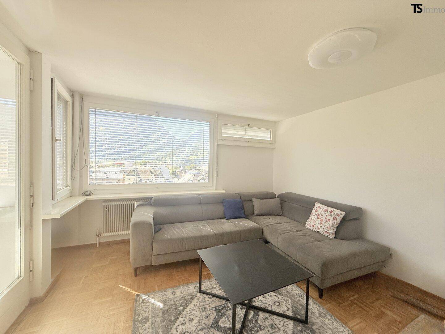 Gemütliches Wohnzimmer mit großem Ecksofa, Couchtisch und klassischem Parkettboden, hell beleuchtet.