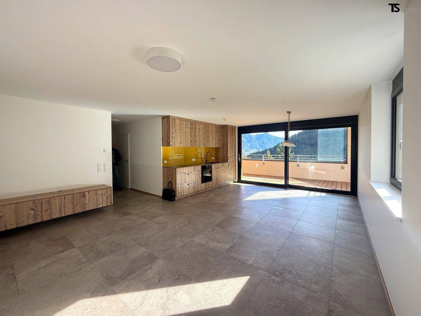 Heller offener Wohnbereich mit integrierter Holzküche und Zugang zum Balkon.