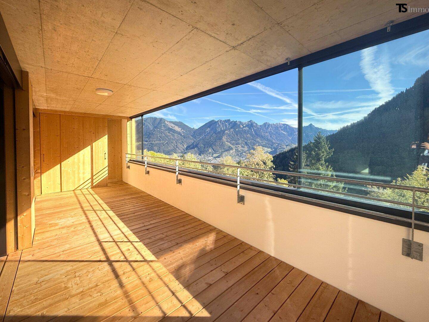 Geräumiger Holzbalkon mit Glasbrüstung und atemberaubendem Panoramablick auf die Berge.