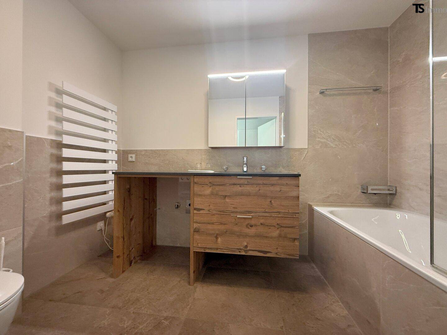 Modernes Badezimmer mit Badewanne, Holzwaschtisch und beheiztem Handtuchhalter.
