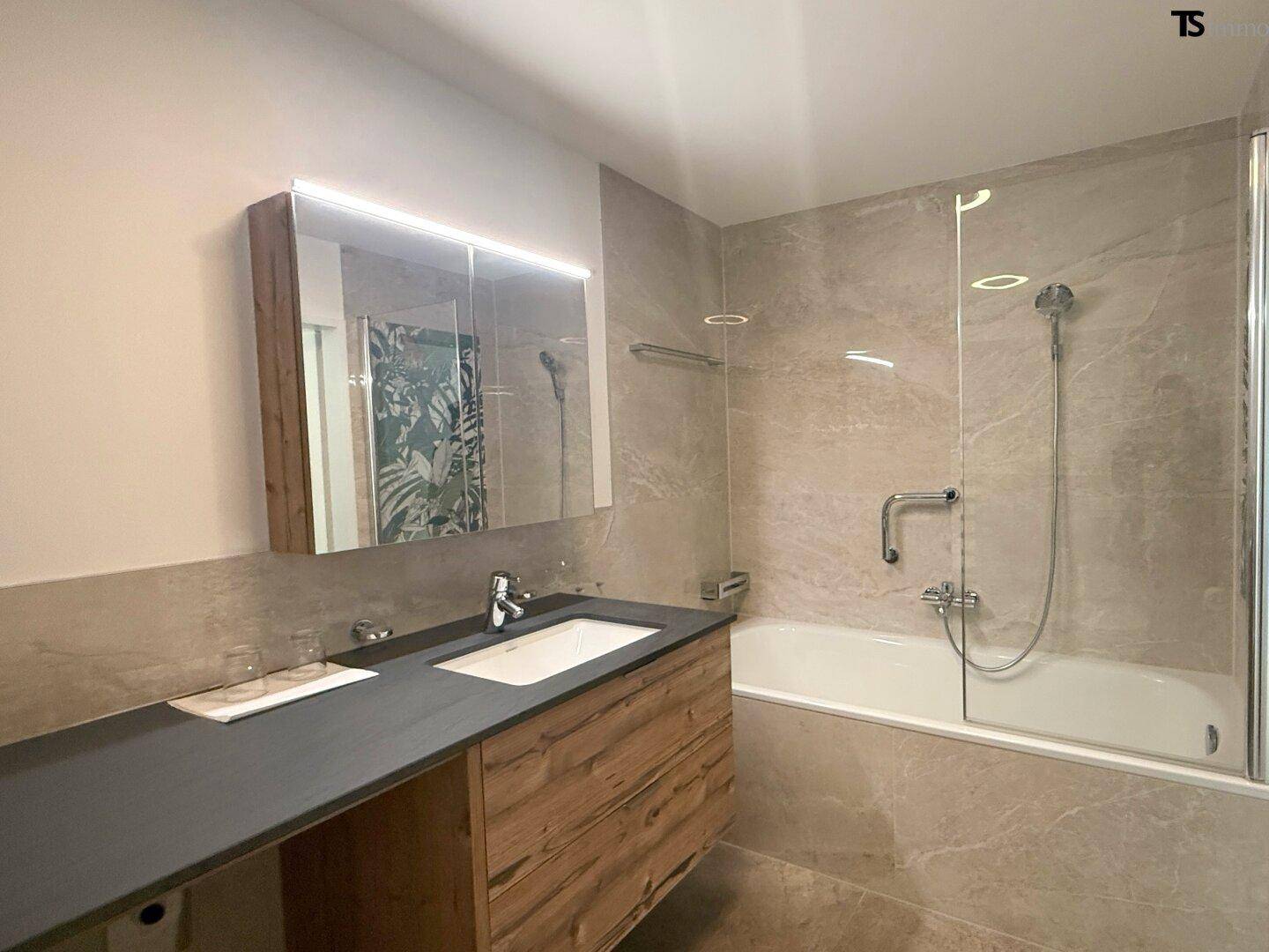Elegantes Badezimmer mit Badewanne, Duschfunktion und modernem Holzwaschtisch.