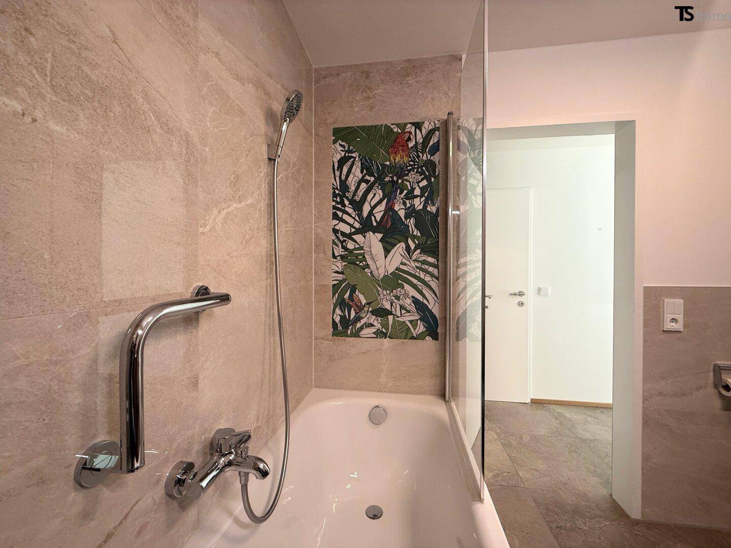Badewanne mit Duschfunktion und Haltegriff in einem modern gefliesten Badezimmer.