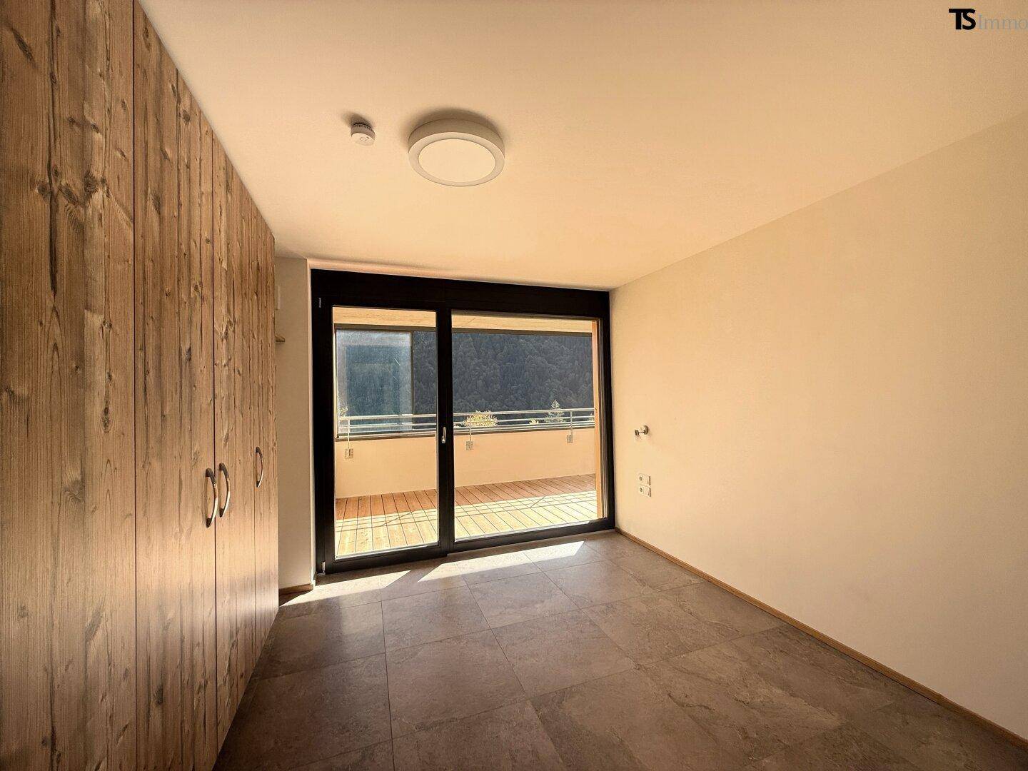 Schlafzimmer mit Holzeinbauschränken, Fliesenboden und Zugang zu einem Balkon.