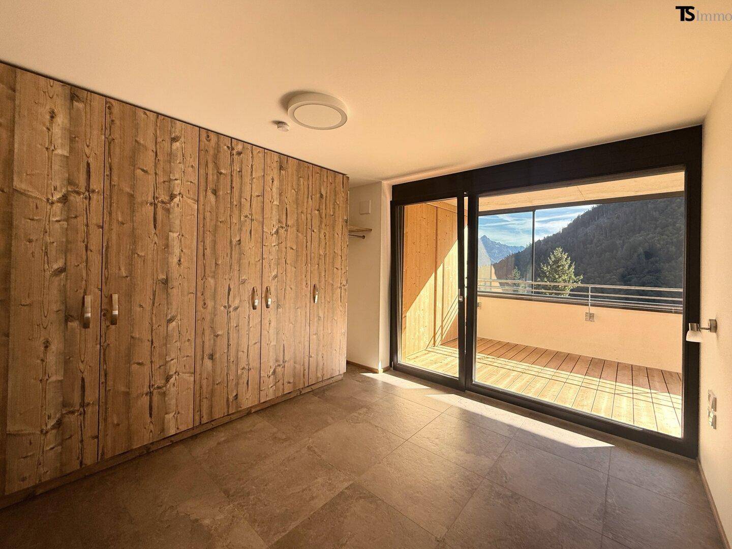 Helles Schlafzimmer mit großen Fenstern, Holzeinbauschränken und Bergblick vom Balkon.