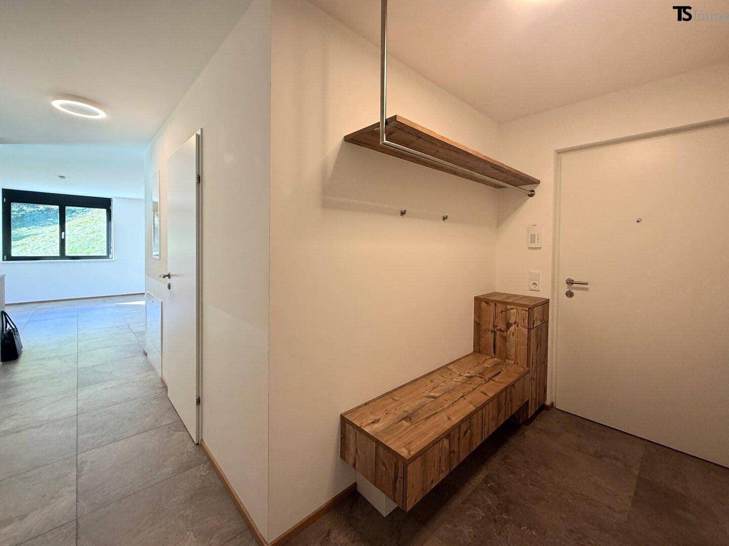 Eingangsbereich mit moderner Holzgarderobe und Fliesenboden, führt zu weiteren Räumen.